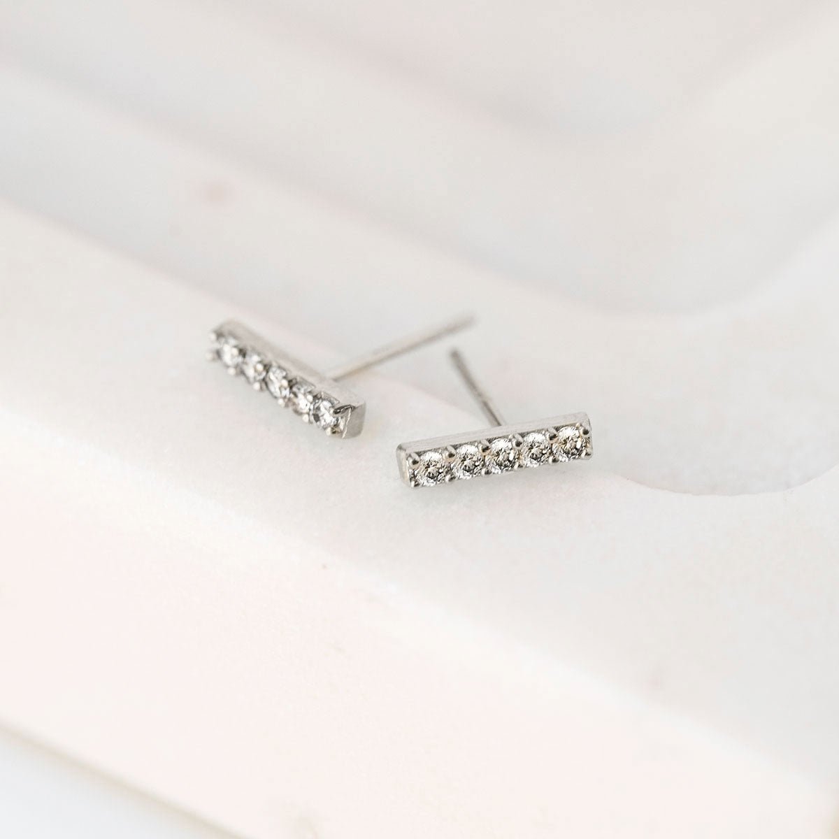 Sterling silver pave bar stud earrings with clear stones, angled close-up on cream marble