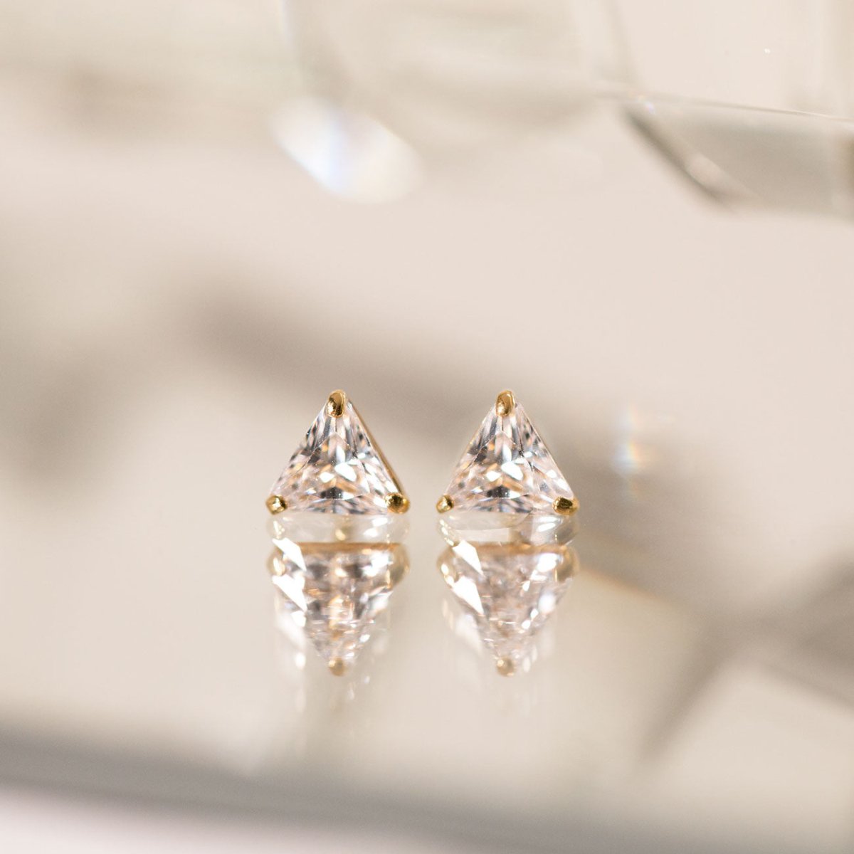 14K gold triangle white zirconia studs, close-up detail on a reflective surface