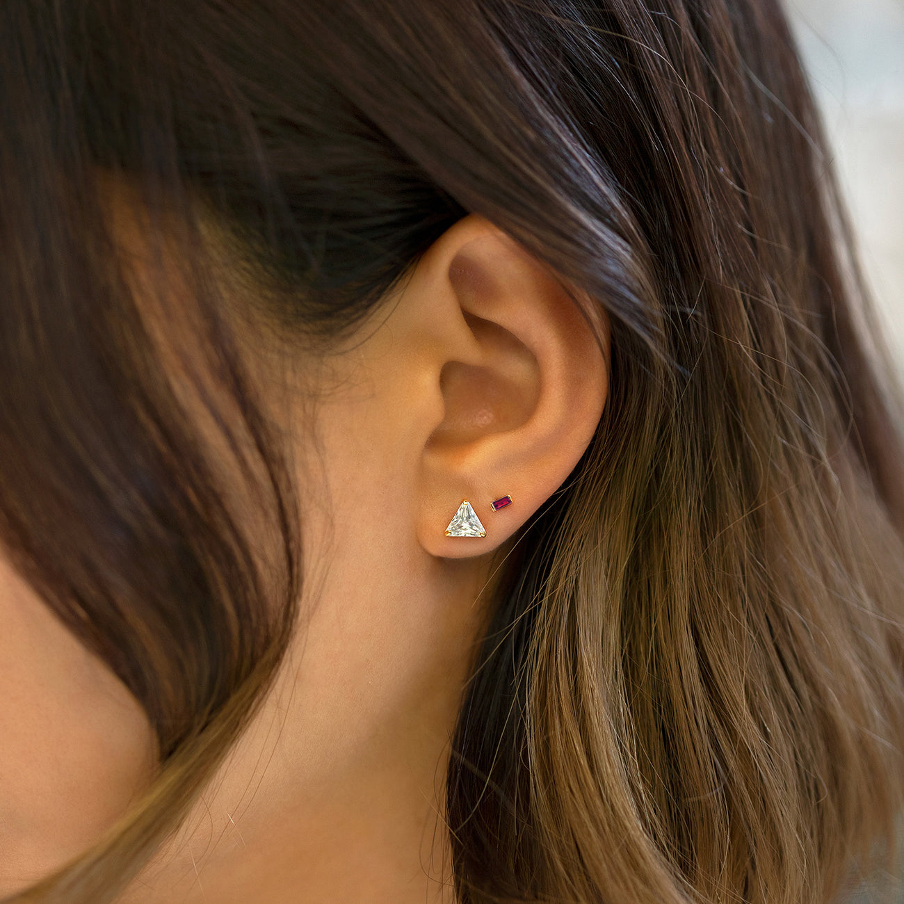 14K gold ruby baguette stud, shown on a model's lobe beside a triangle clear-stone stud