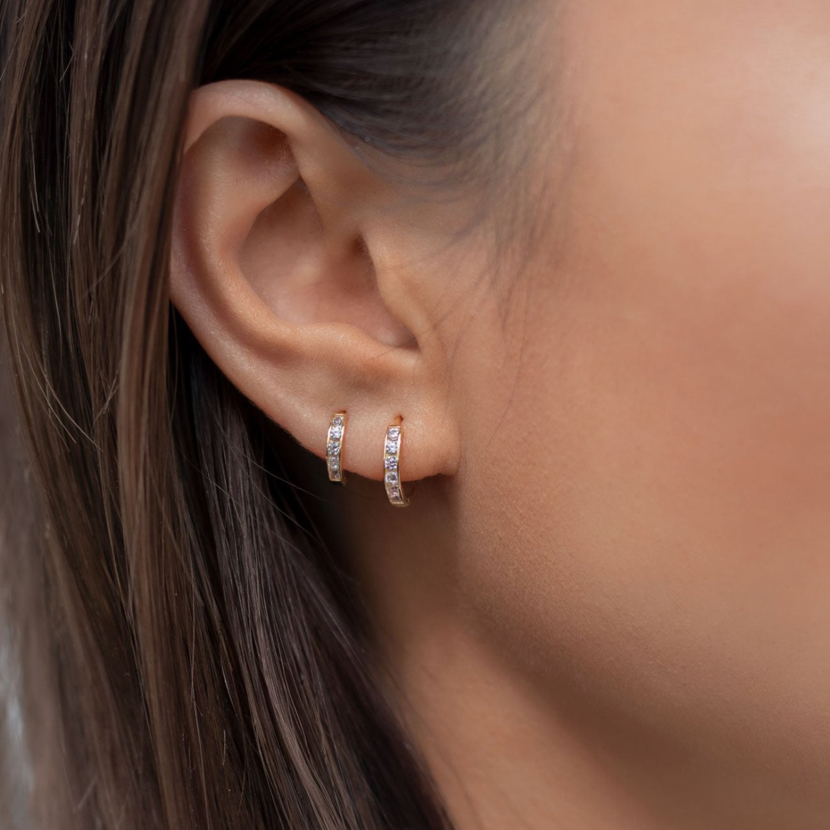 Gold vermeil huggie hoops with round clear cubic zirconia shown on a model's earlobe