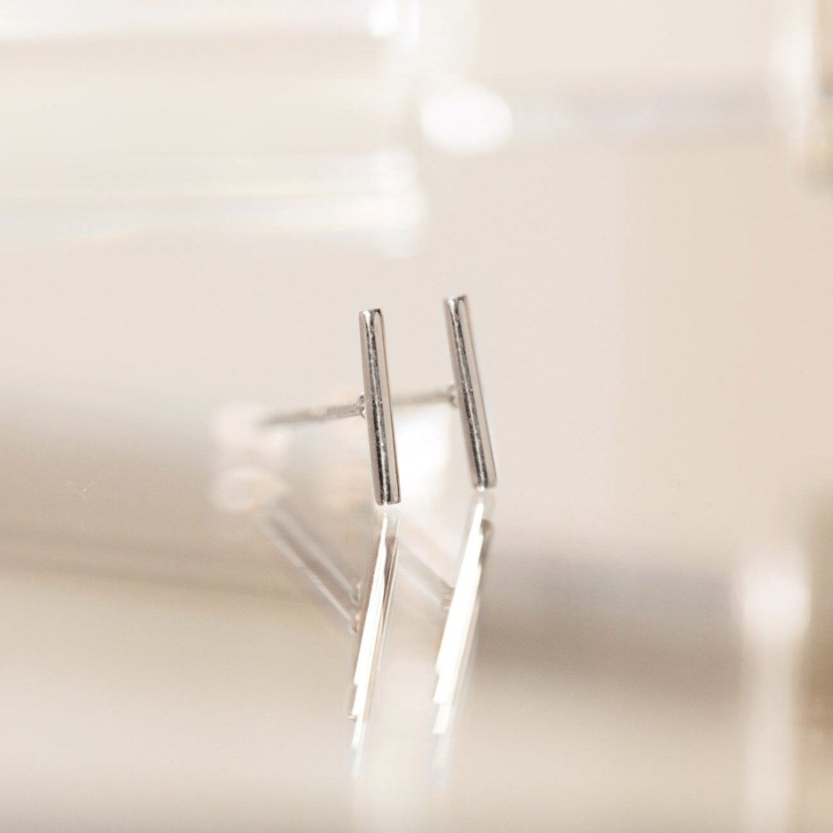 14K white gold thin bar stud earrings standing upright, close-up on a soft white surface