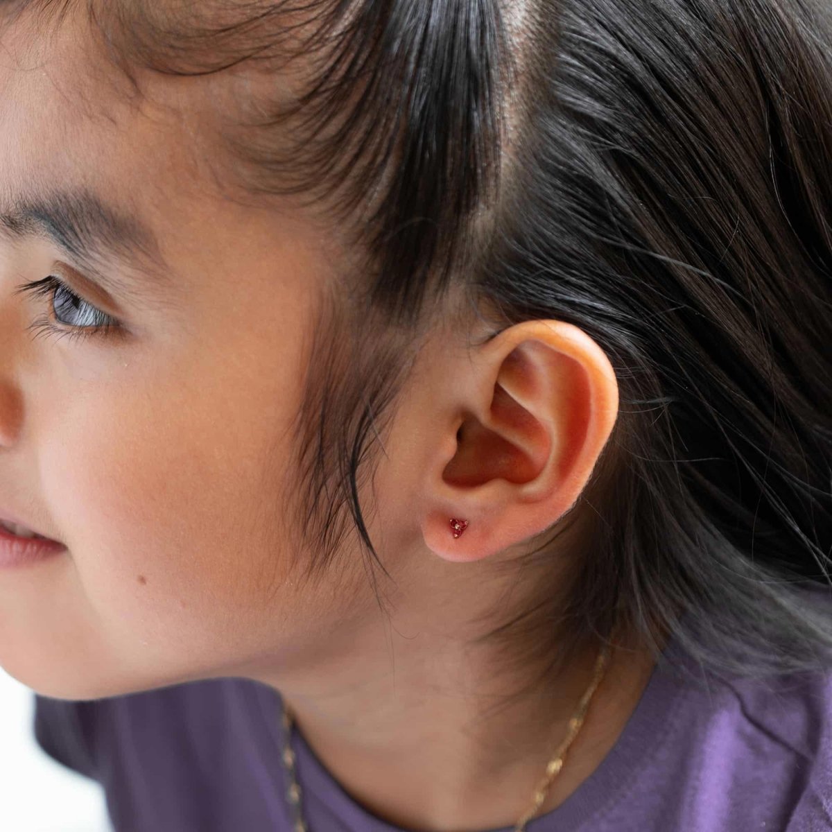 14K gold red garnet clover stud shown in a child's earlobe, side profile view