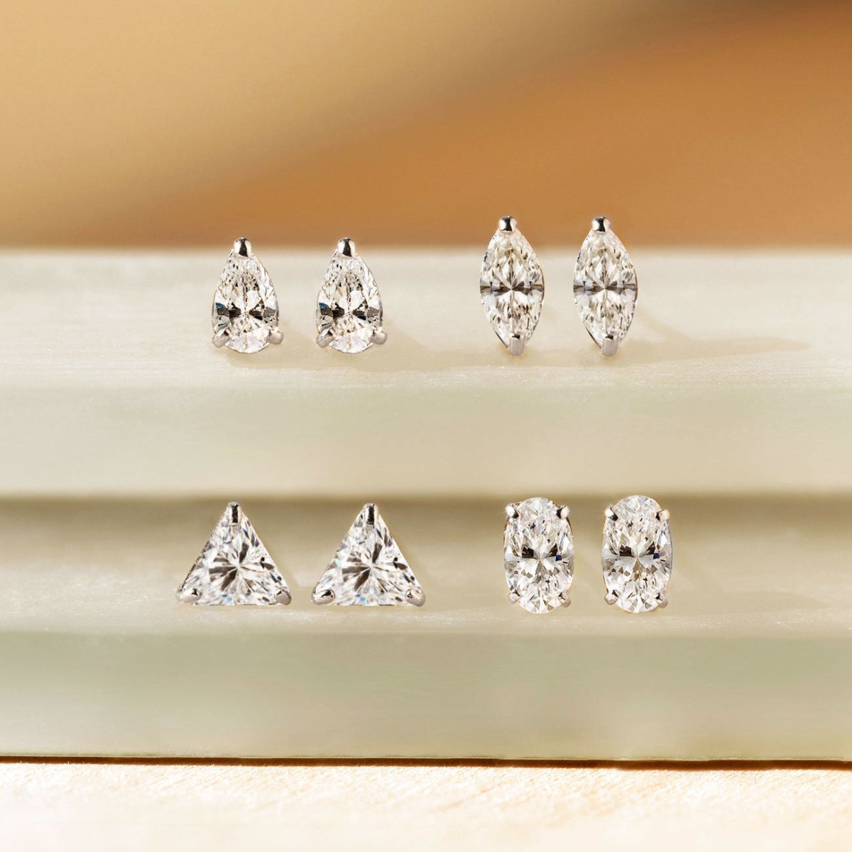 14K white gold stud earrings with clear pear, marquise, triangle and oval stones, on a pale green ledge