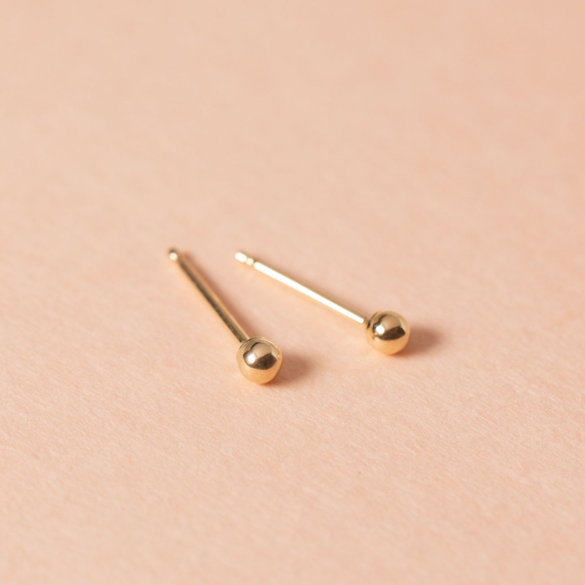 Pair of gold-filled tiny ball studs with long posts, on a cream background