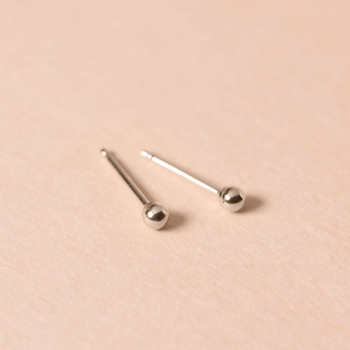 Pair of sterling silver tiny ball studs with long posts, on a cream background