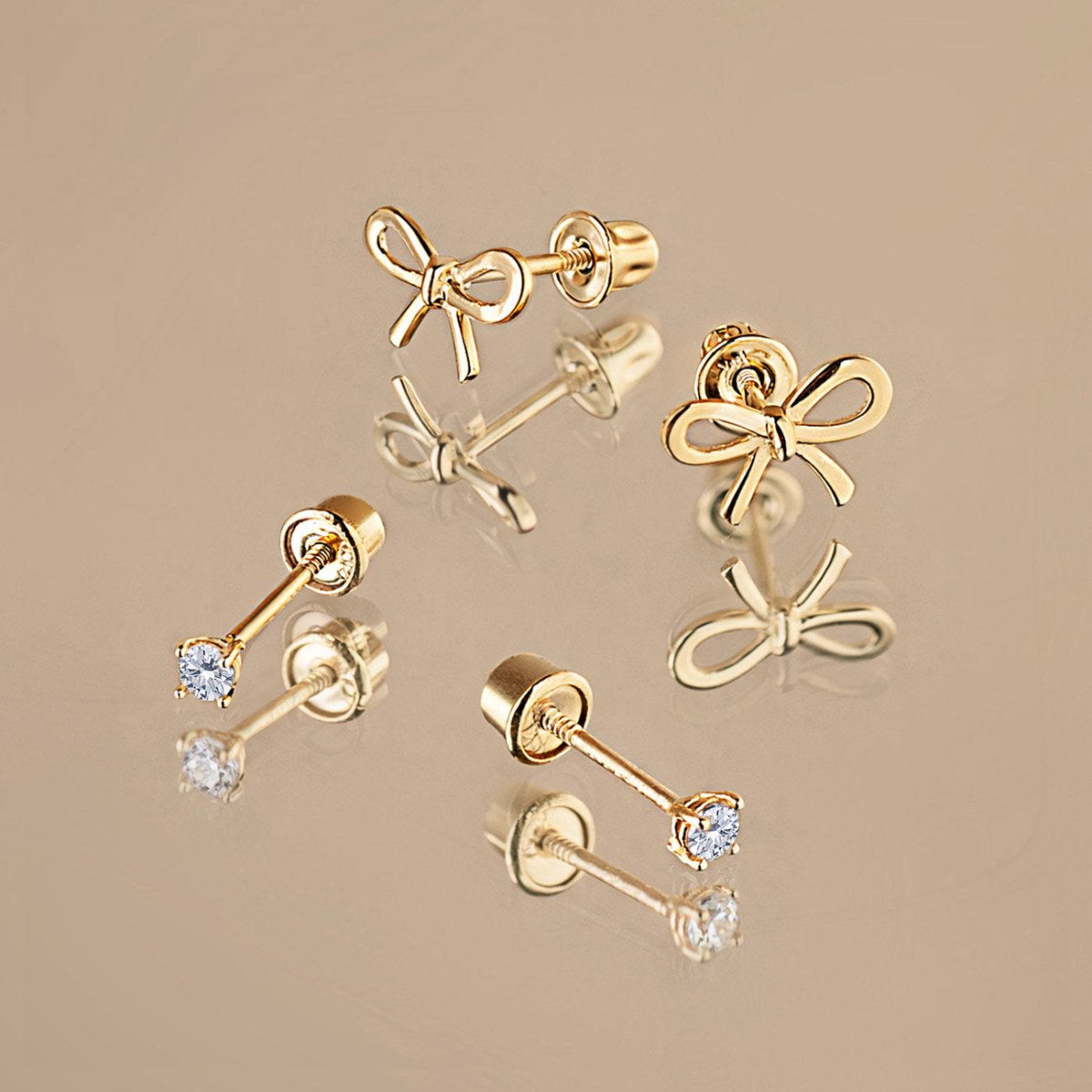 14K gold screw-back studs including bow shapes and round clear white sapphire solitaires, on a cream background
