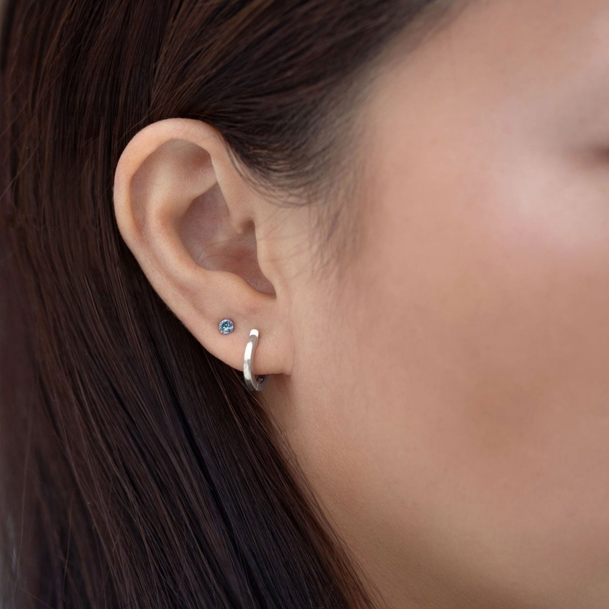 14K white gold blue zircon tiny stud with an aqua-blue stone, shown on a model's lobe