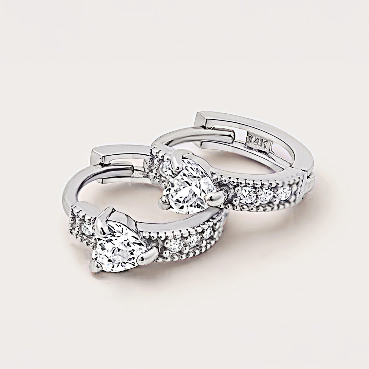 14K white gold heart huggie hoops with white zirconia stones, close-up detail on a cream background