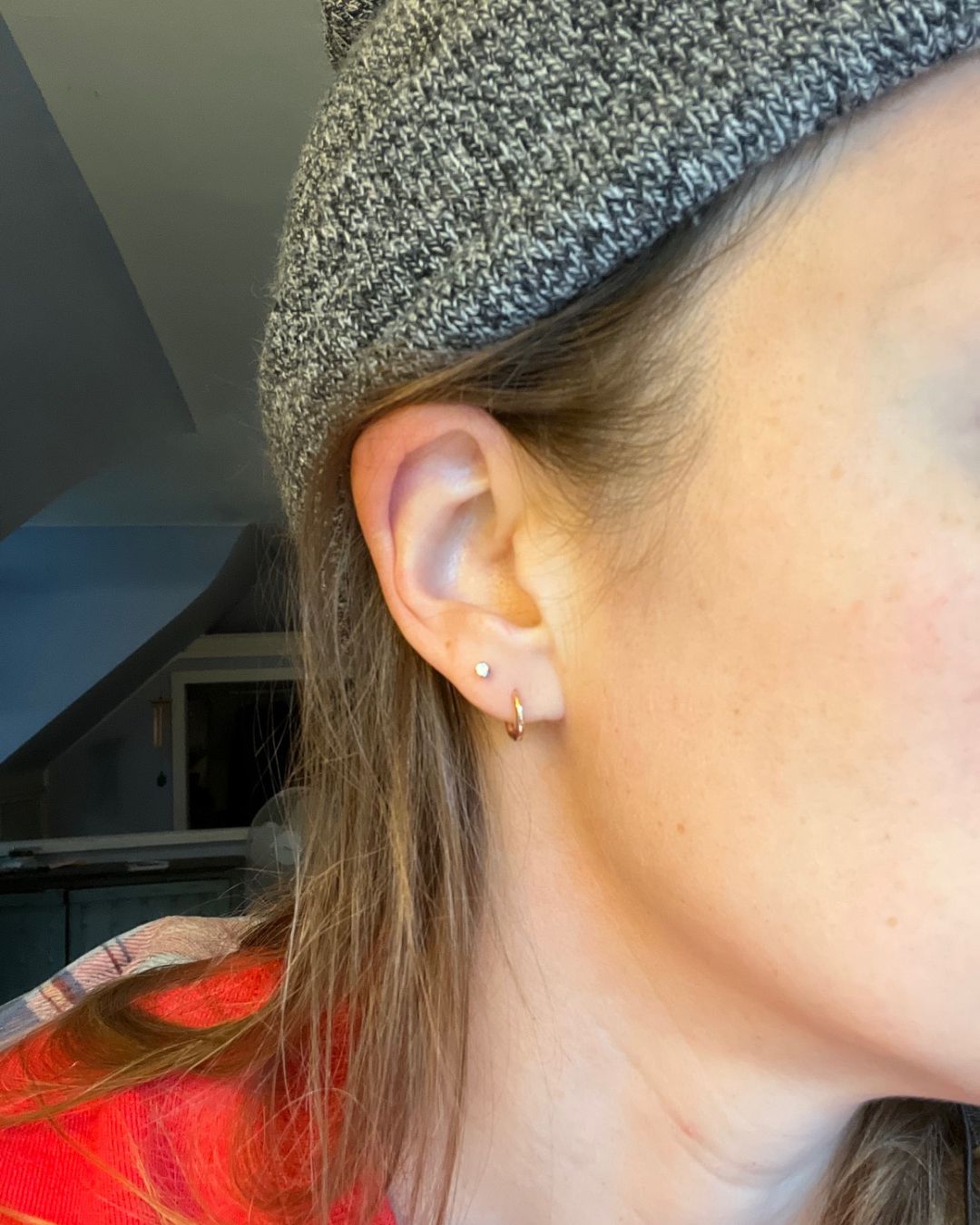 Close-up of an ear with a small gold huggie hoop in the lobe and a tiny stud stud above it