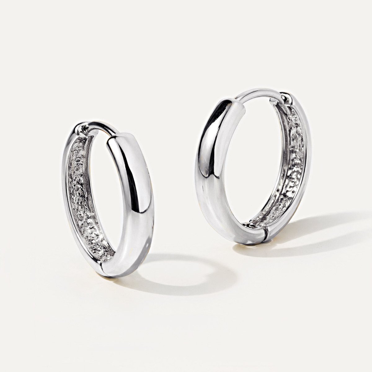 14K white gold mini huggie hoops with a hinged closure, shown at an angle on a white background