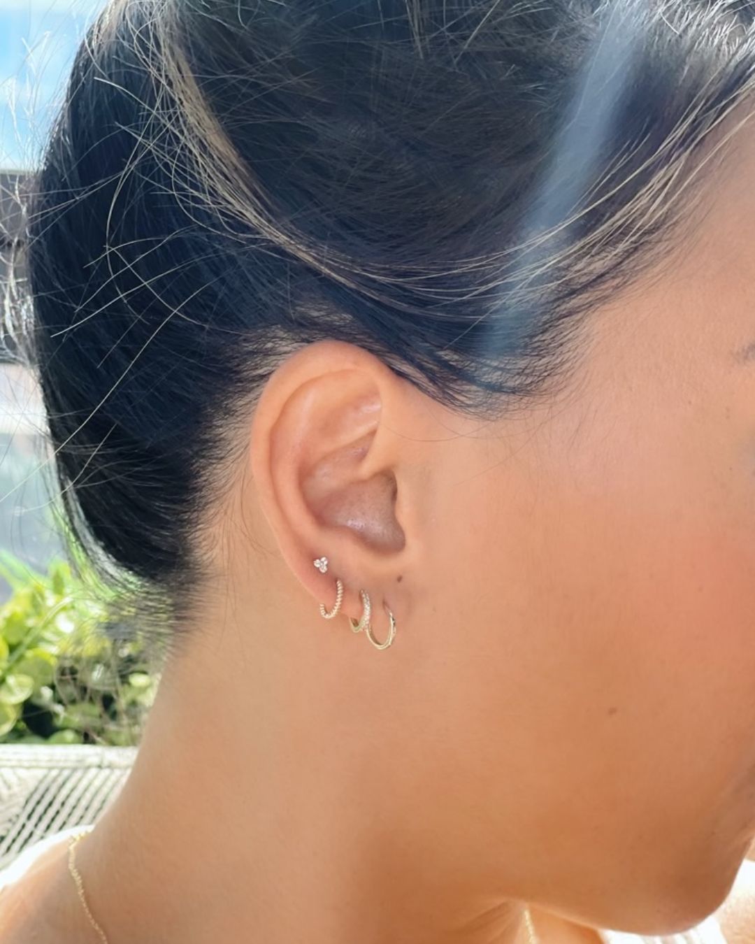 Ear worn with a tiny three-stone cluster stud, a crystal-set gold hoop and a plain gold hoop in the lobe