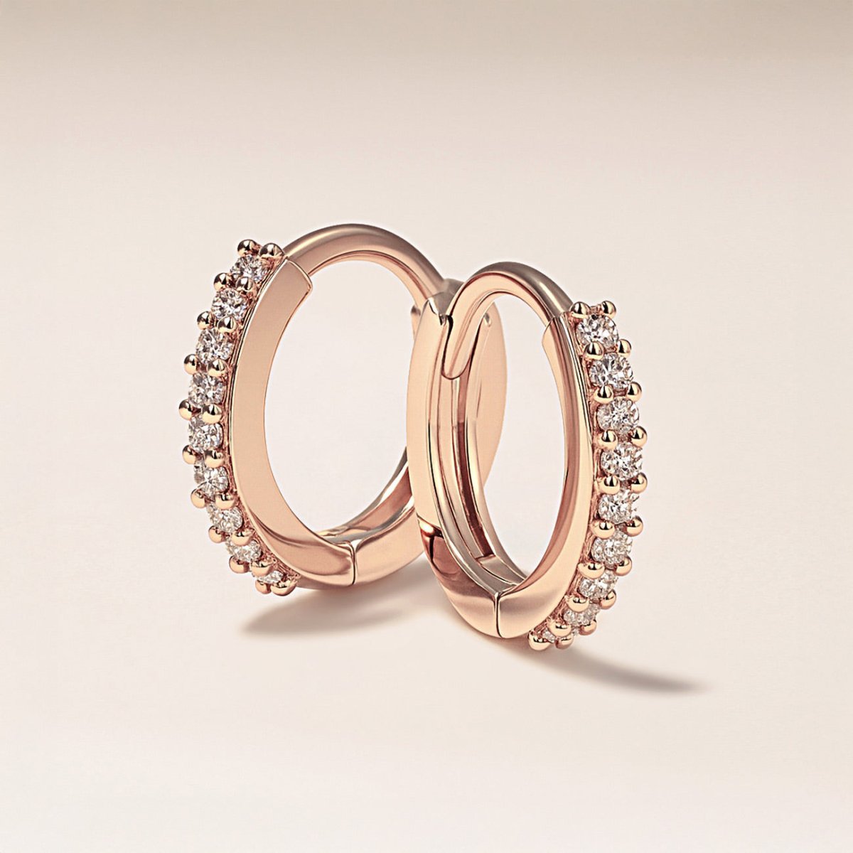 Pair of rose gold vermeil pavé huggie hoops with round clear stones, angled on a cream background