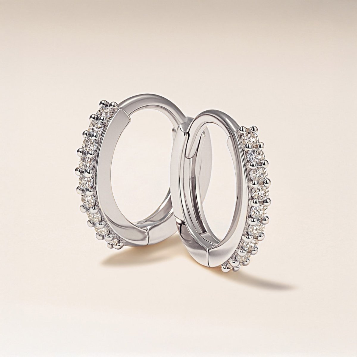 Pair of sterling silver pavé huggie hoops with round clear stones, angled on a cream background