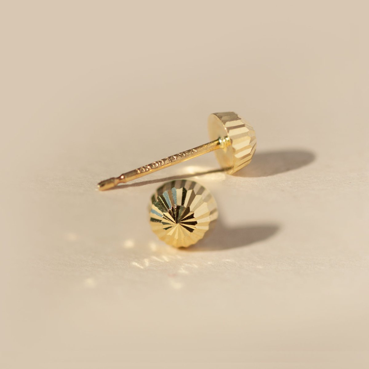 14K gold faceted ball stud earrings showing front and post, on a cream background