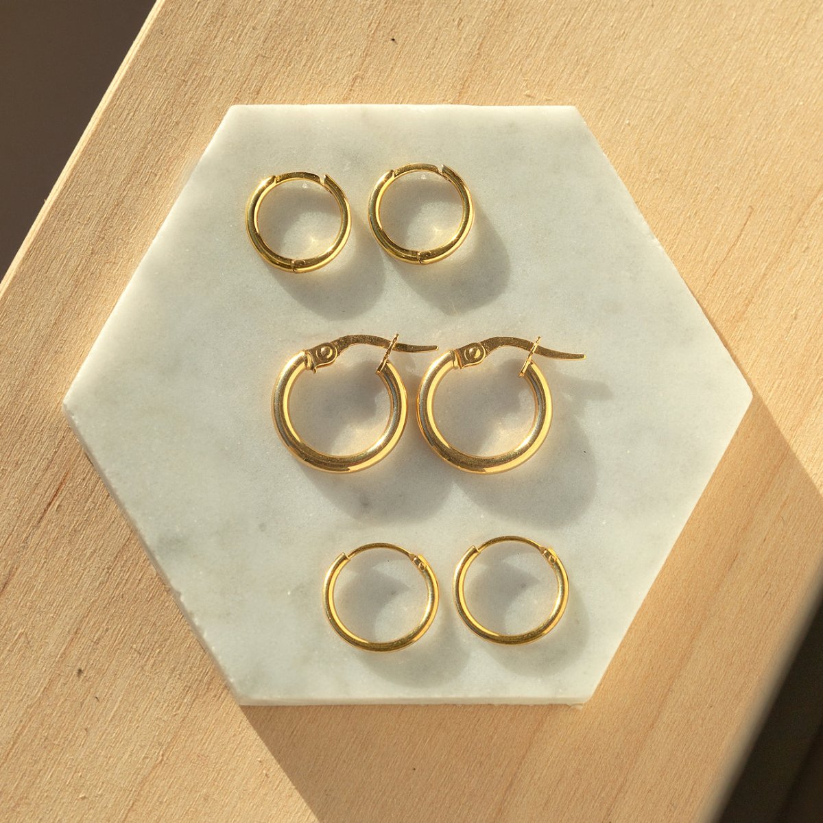 Three pairs of gold vermeil small hoop earrings in graduated sizes, on white marble