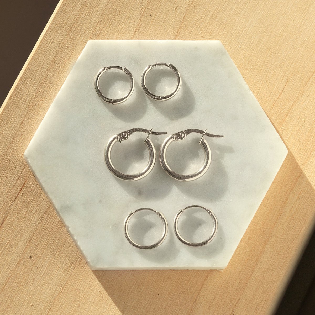 Three pairs of sterling silver small hoop earrings in graduated sizes, on white marble