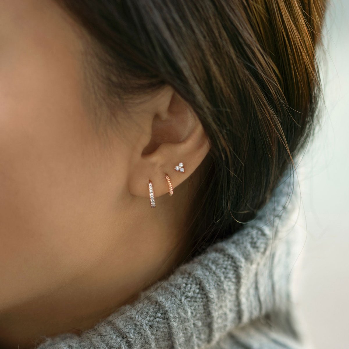 Close up of woman's ear featuring 14K Rose Gold Tiny Clover Pave Stud and huggie earrings