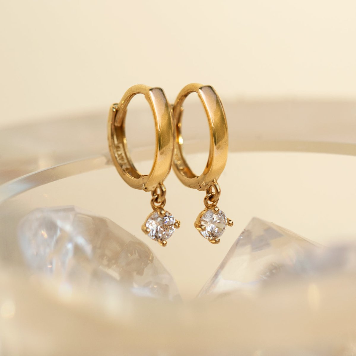 14K gold huggie hoops with round moissanite dangles, close-up resting on clear crystals