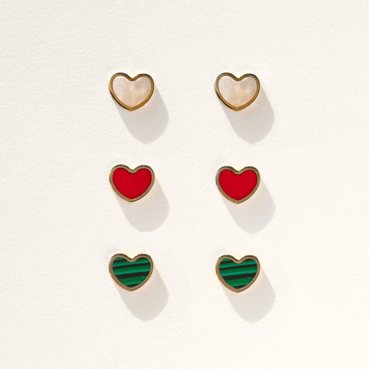 14K gold heart studs with red carnelian inlay shown among other red stud styles on a white background