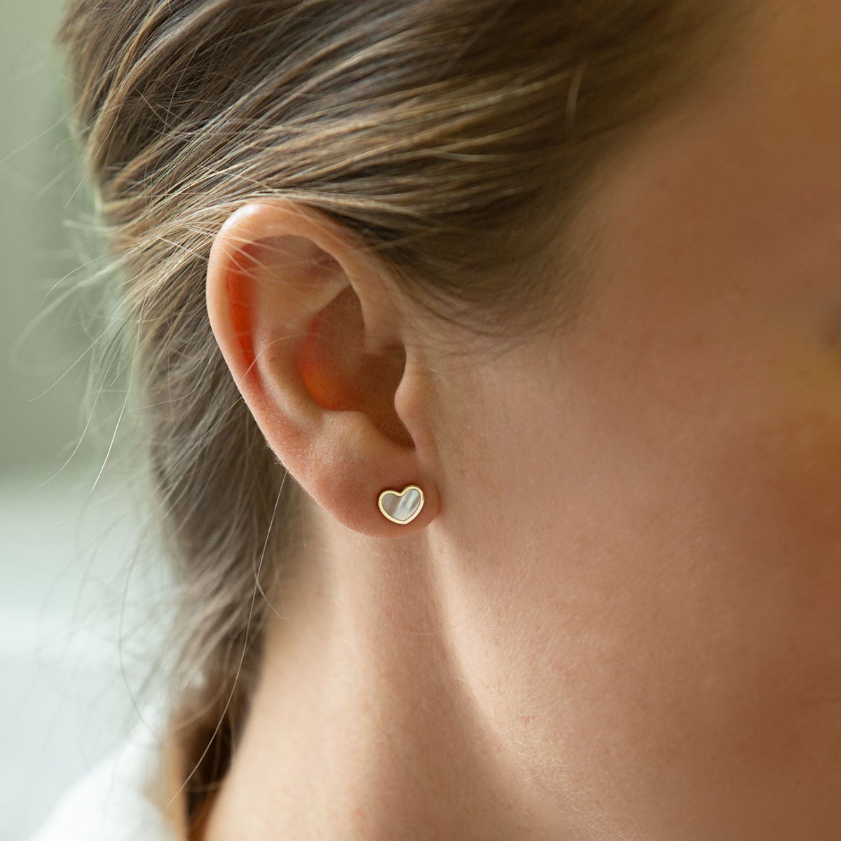 14K gold heart stud with mother of pearl inlay, shown on a model's earlobe