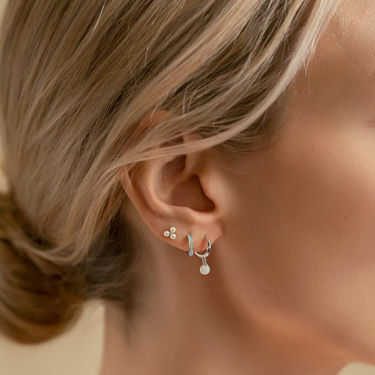 14K white gold trinity pearl stud shown on a model's lobe with silver hoops