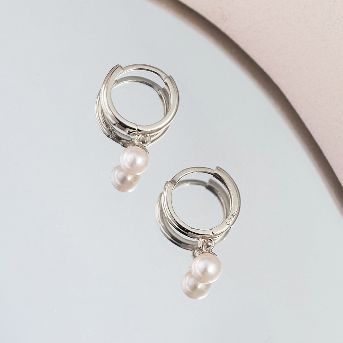 14K white gold huggie hoop earrings with two pearl drops, on a pale gray surface
