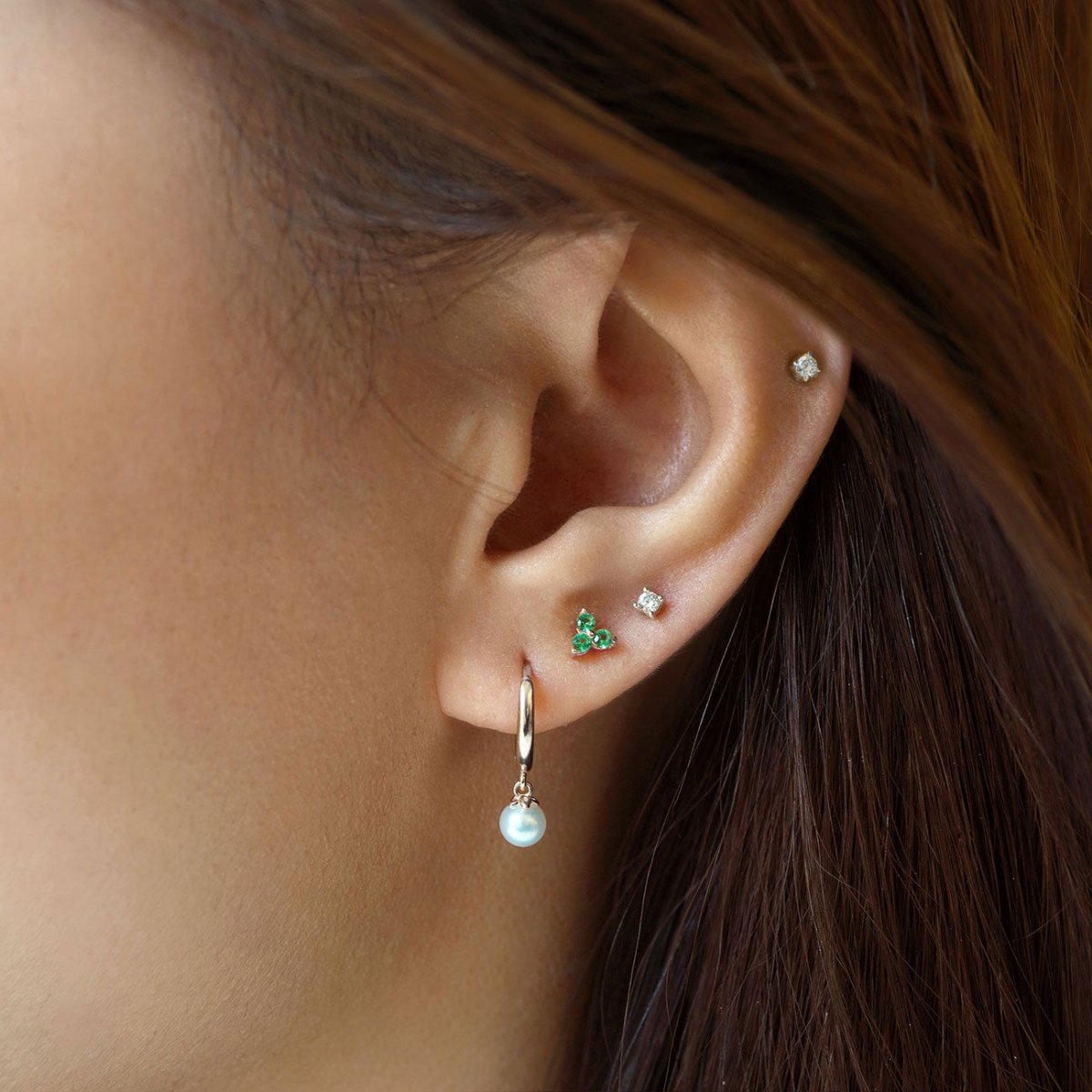14K white gold huggie hoop with a dangling pearl, shown on a model's lobe in a styled ear stack