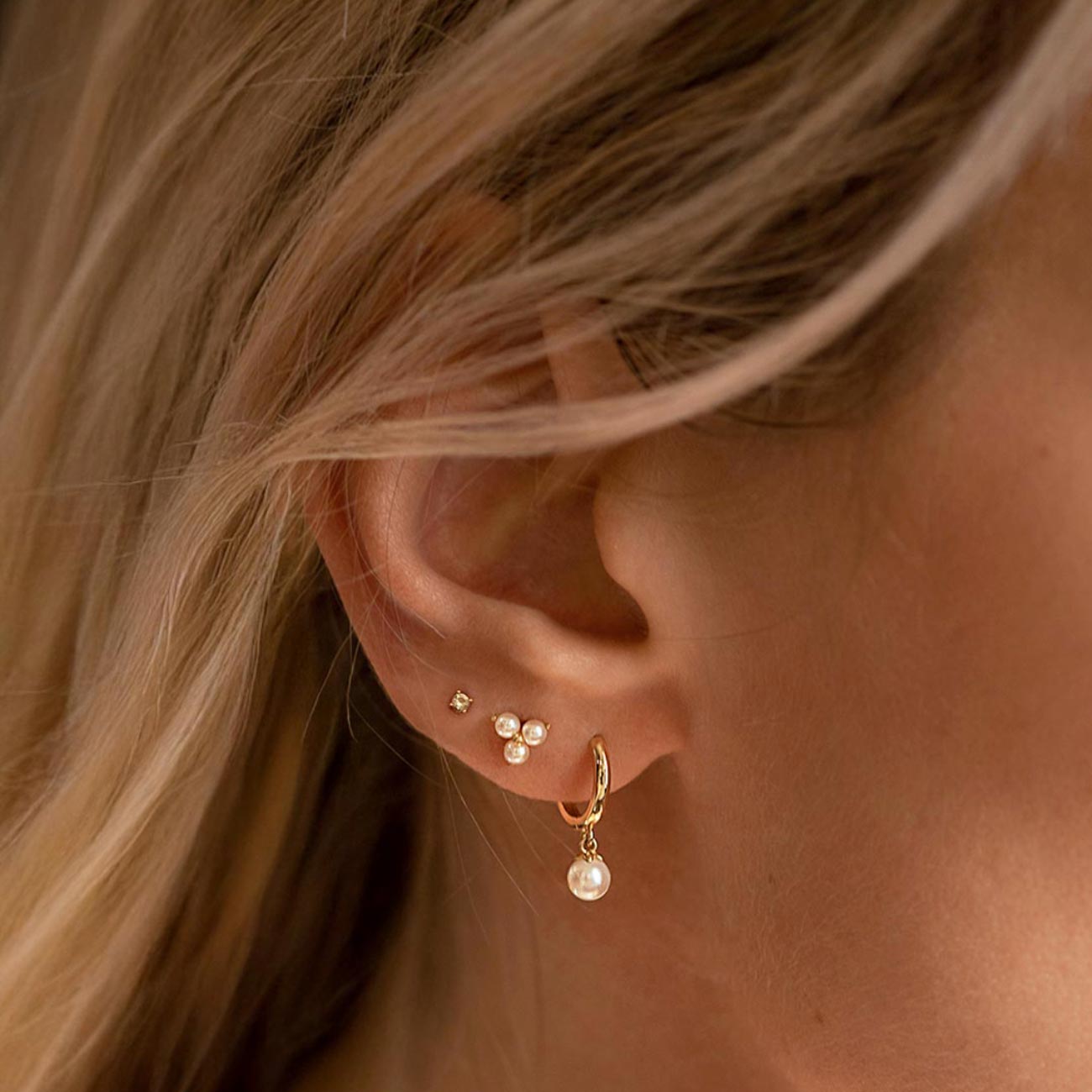 14K gold pearl-drop huggie hoop and tiny studs shown on a model's lobe