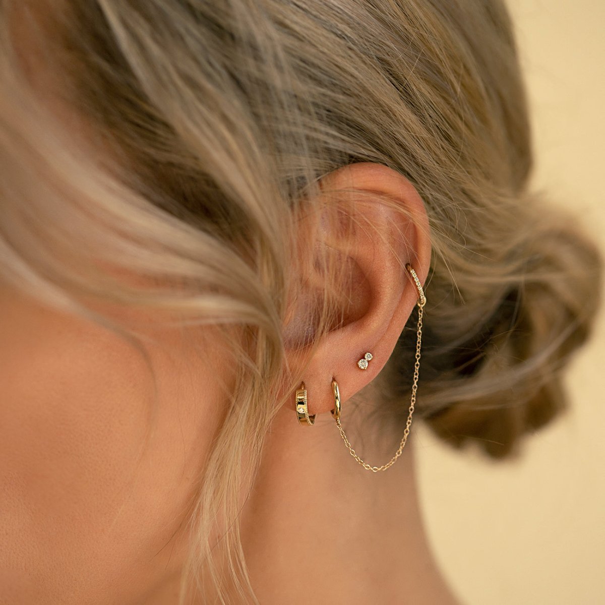 14K gold milgrain band huggie hoop with a white sapphire, styled in a gold ear stack