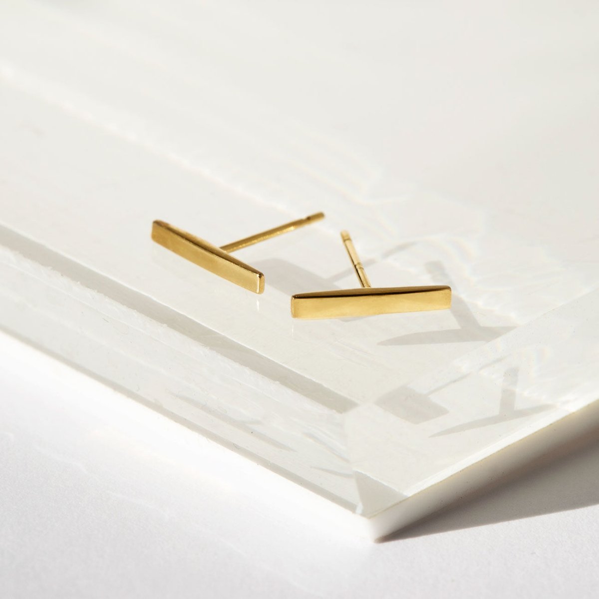 14K gold bar stud earrings shown at an angle on a white tray, posts visible