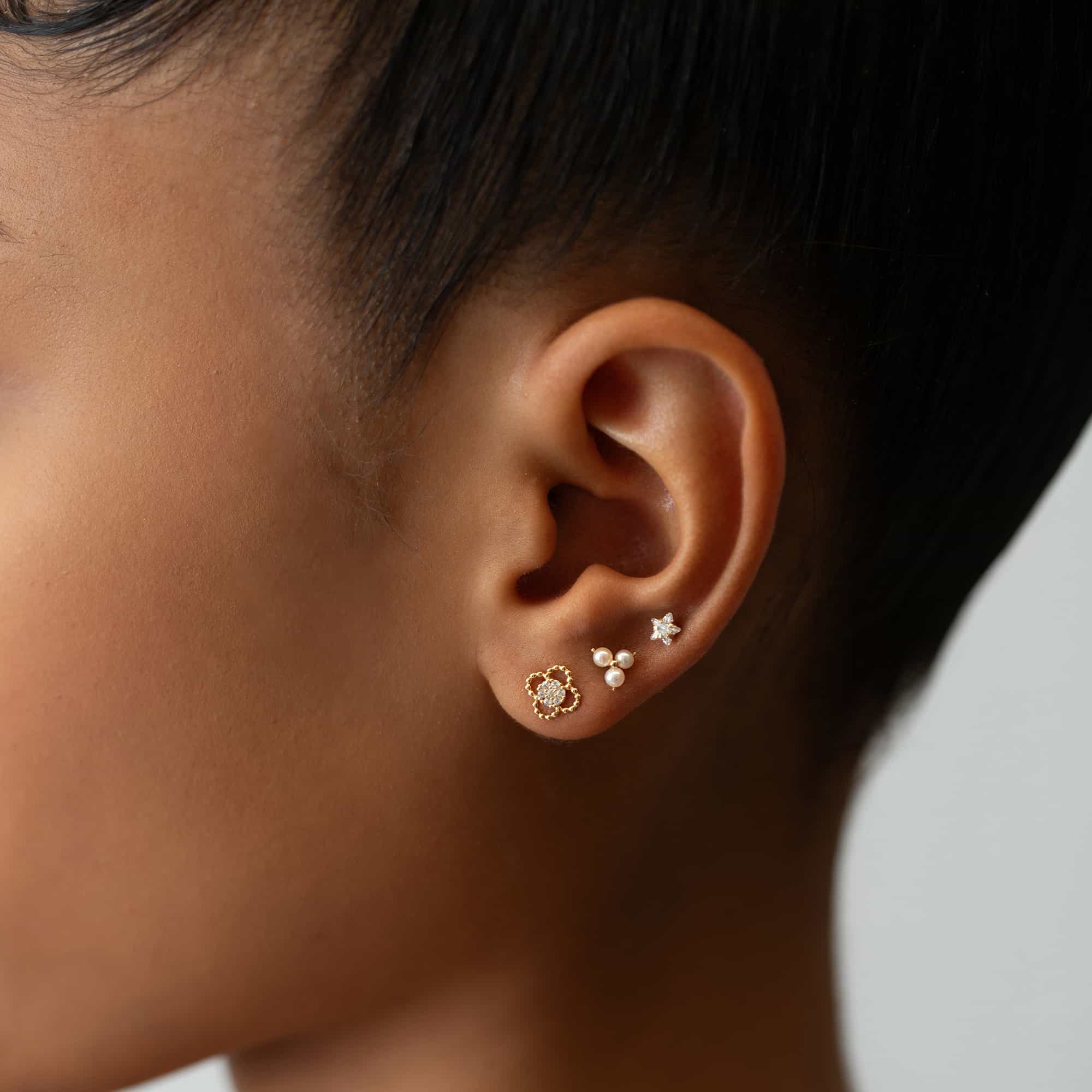 14K gold clover stud with a beaded outline and pave white zirconia center, shown on a model's lobe