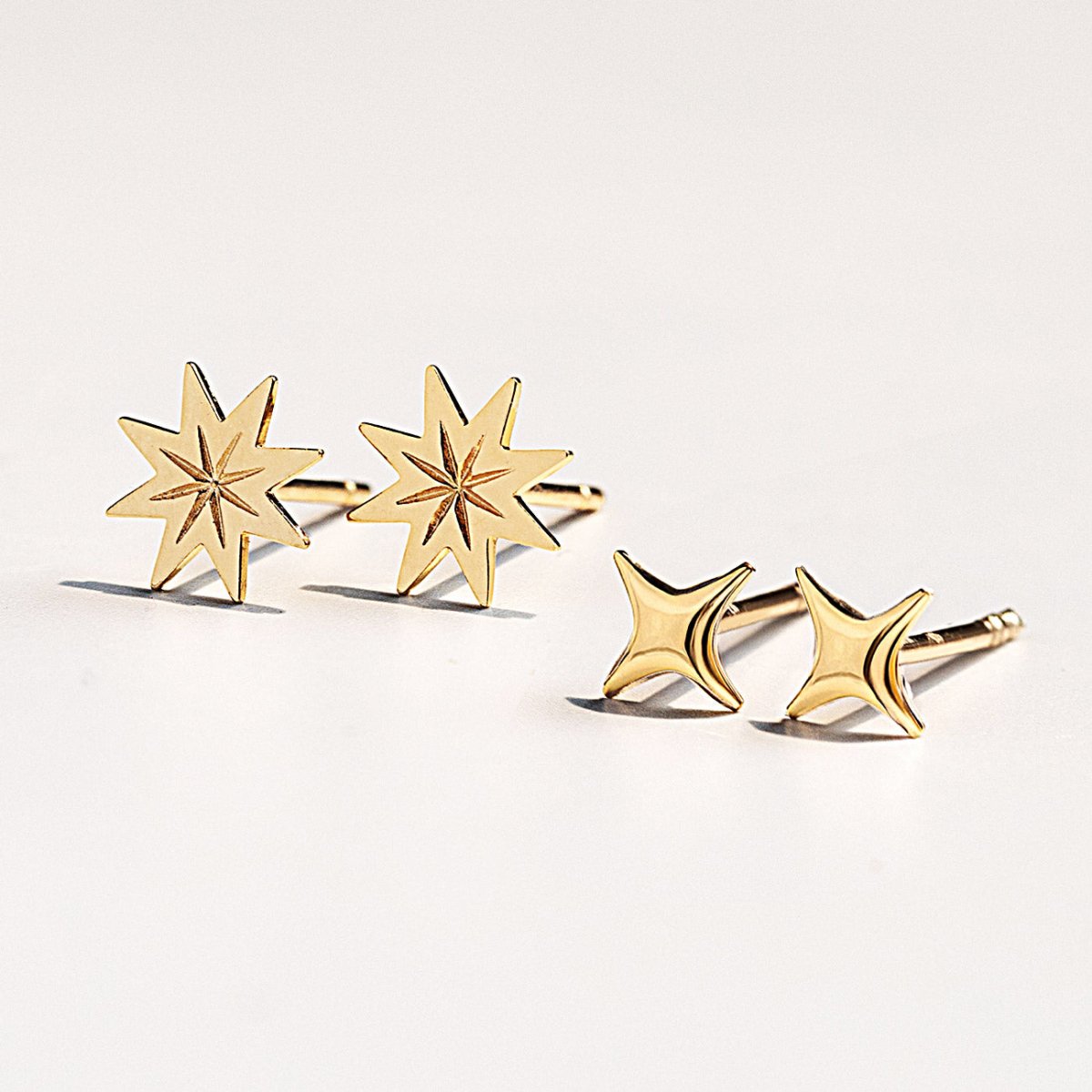 Gold eight-point starburst studs beside smaller four-point star studs, on a white background