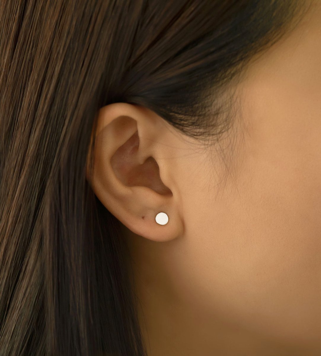 Sterling silver flat round disc stud earring shown on a model's lobe, close-up detail