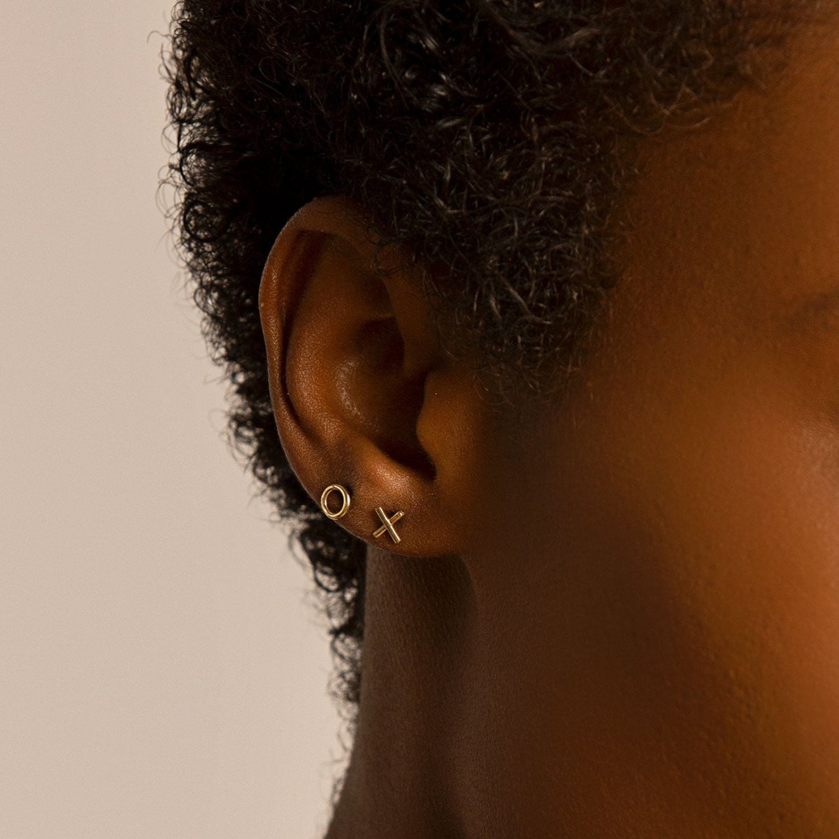 14K gold XO stud earrings shown on a model's lobe in an O and X stack