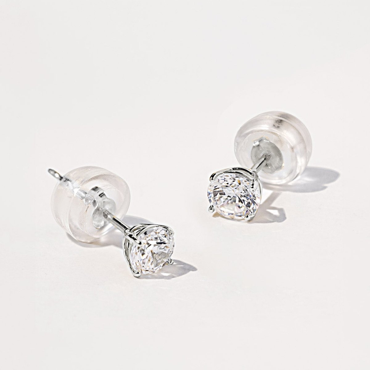 14K white gold white sapphire stud with a silicone back, close-up on a white surface