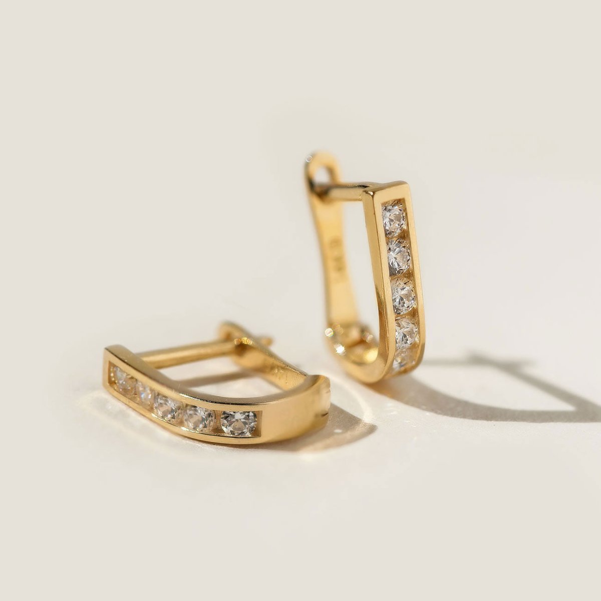 14K gold huggie hoops channel-set with clear white zirconia, close-up detail on a cream background