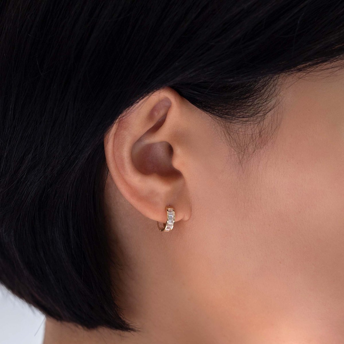 14K gold baguette huggie hoop with clear stones, shown on a model's lower lobe