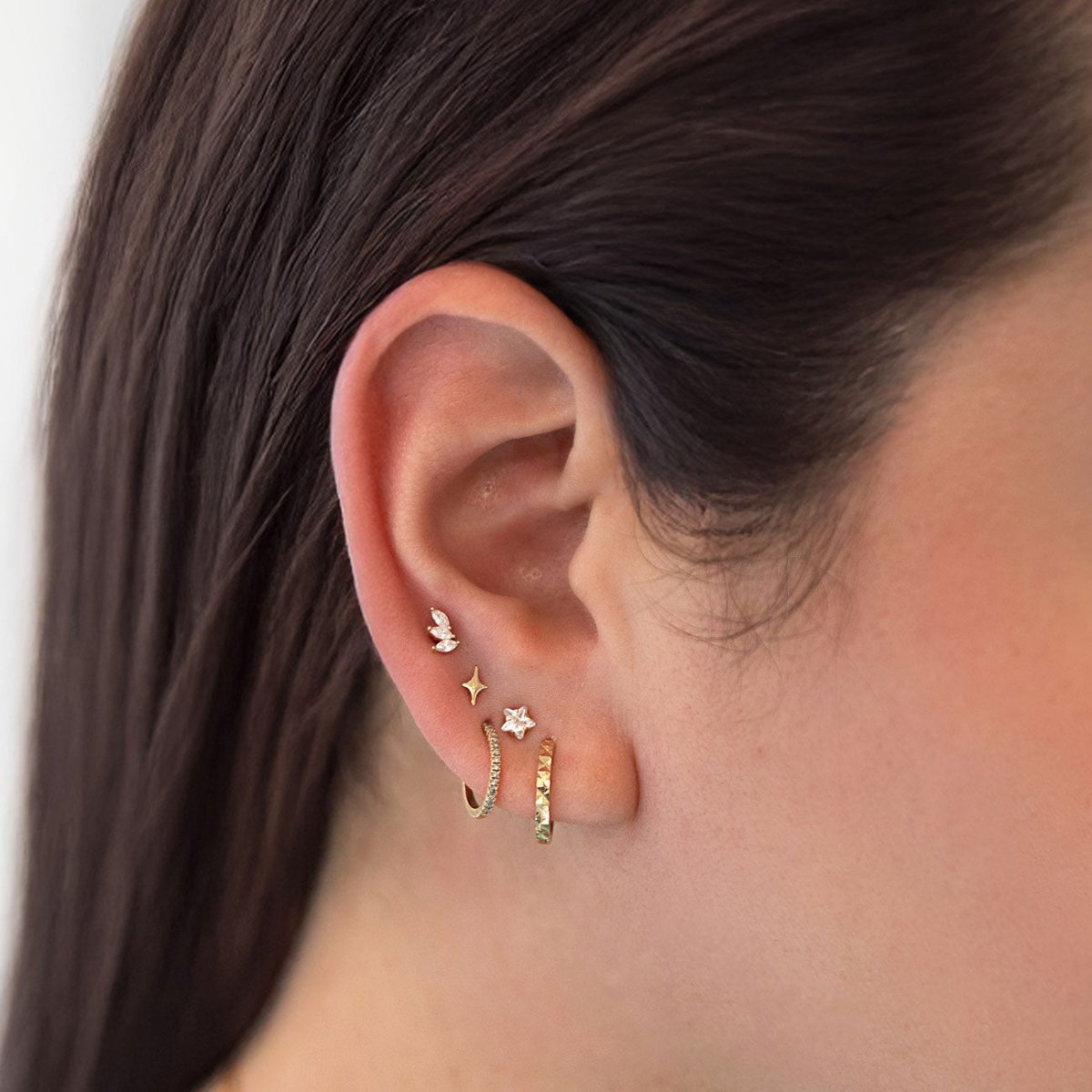 Gold pavé huggie hoops with butterfly and star flat back studs, shown in a stack on a model's ear