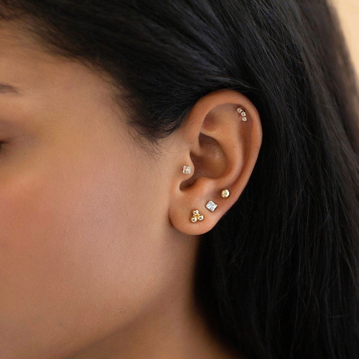 Gold faceted ball and clear stone studs shown stacked on a model's ear