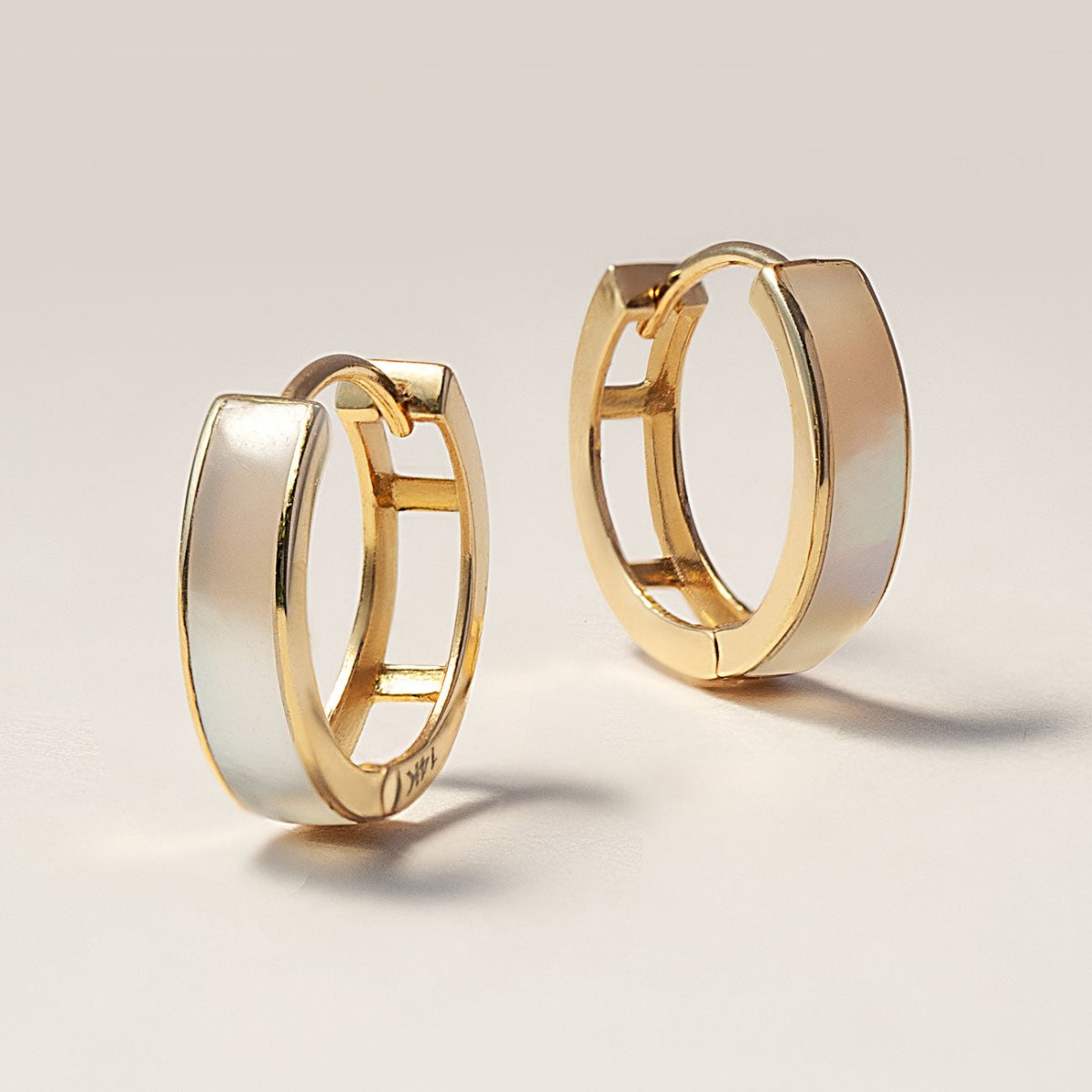 14K gold mother of pearl huggie hoops with a glossy white inlay, on a cream background