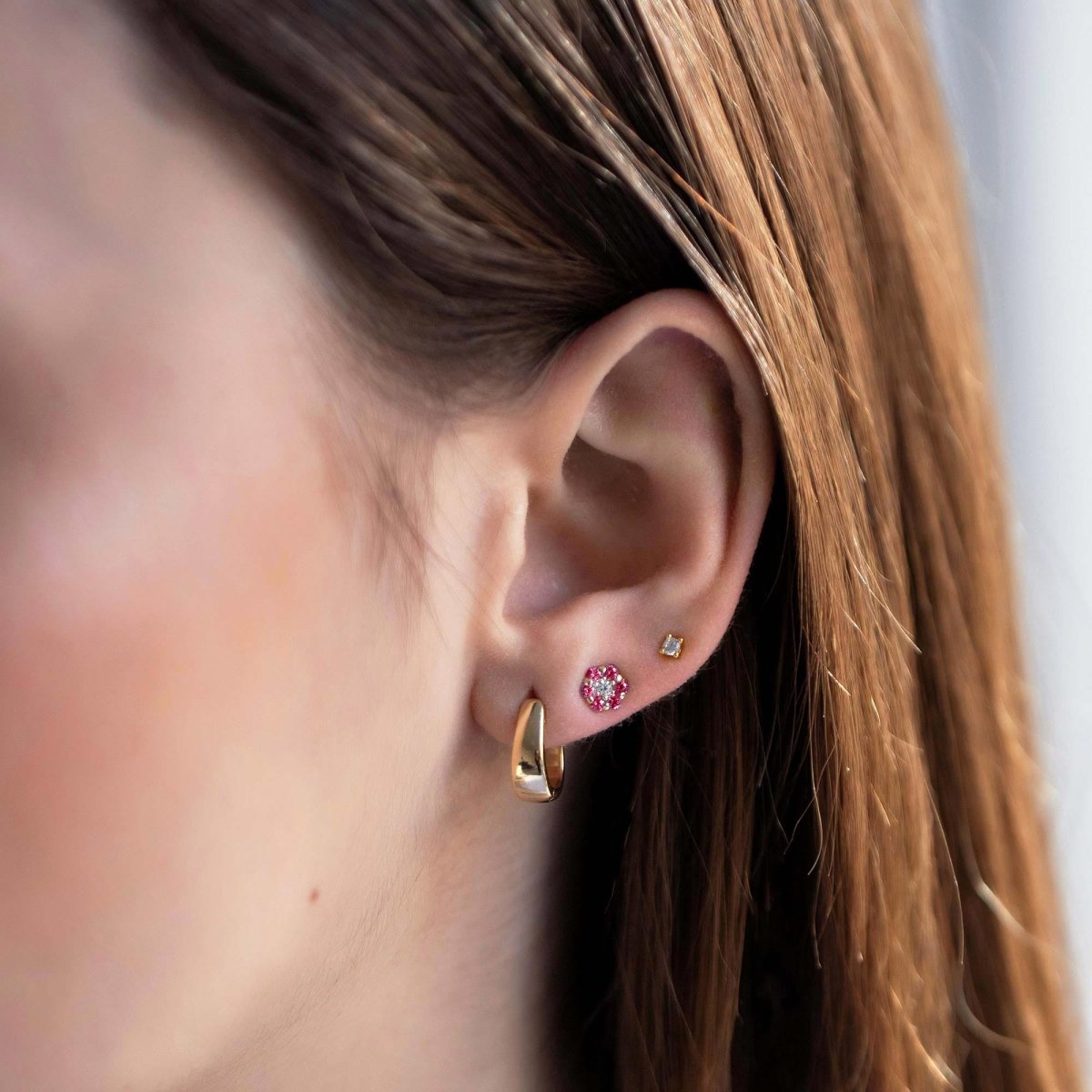 14K gold ruby cluster flower stud shown on a model's lobe alongside a gold huggie hoop