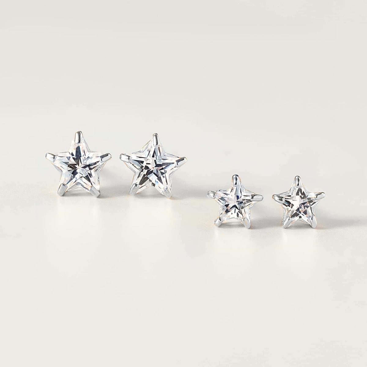 Two sizes of 14K white gold star studs with faceted clear zirconia stones, on a cream background