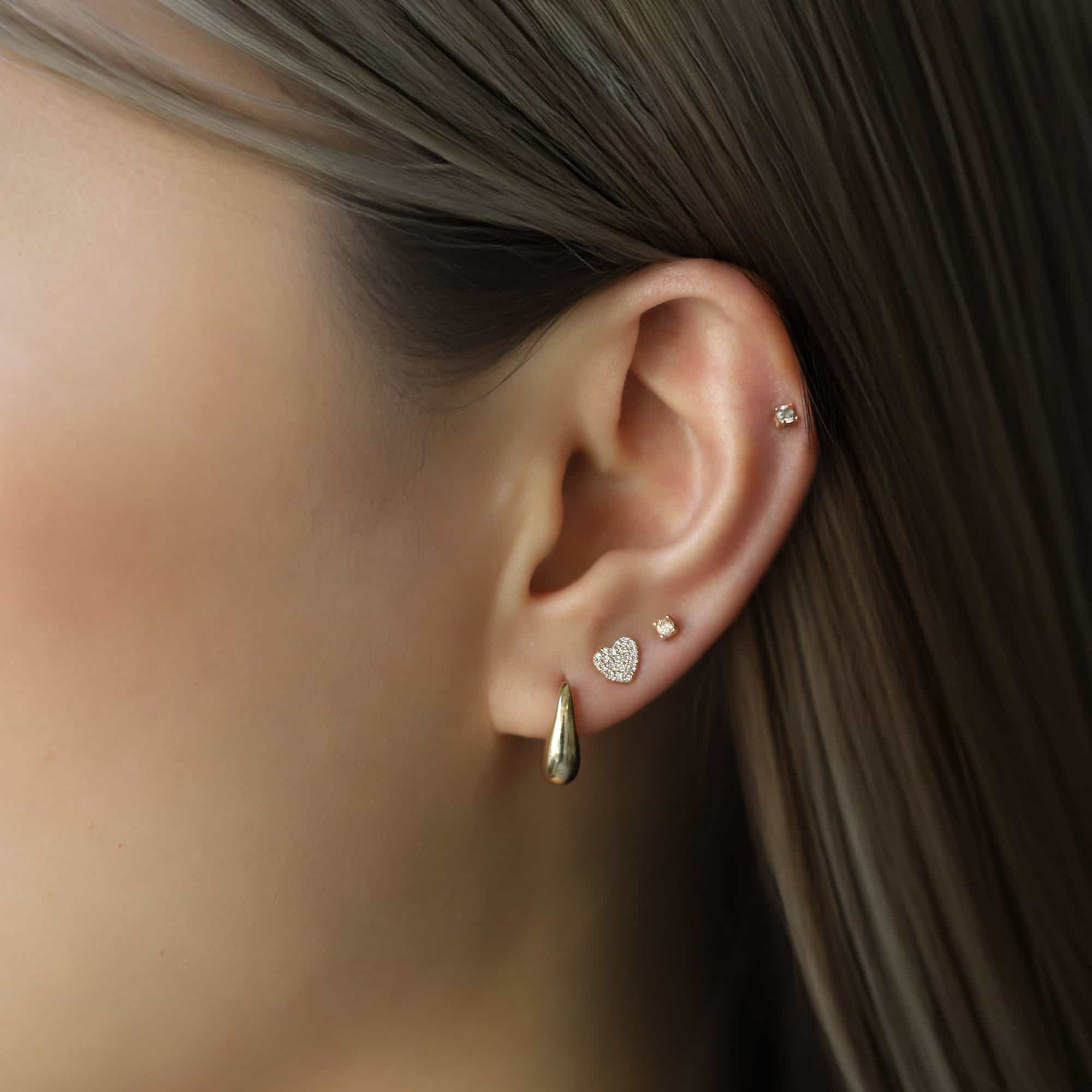 Gold heart stud, tiny stud and teardrop earring styled in a lobe and helix ear stack on a model