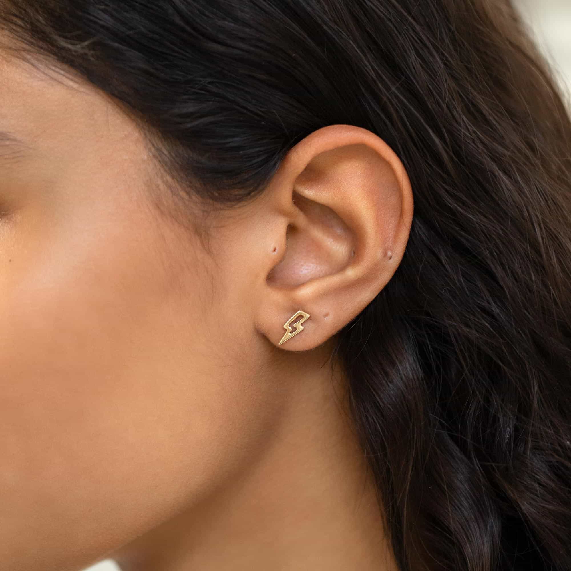 14K gold open lightning bolt outline stud earring shown on a model's lobe