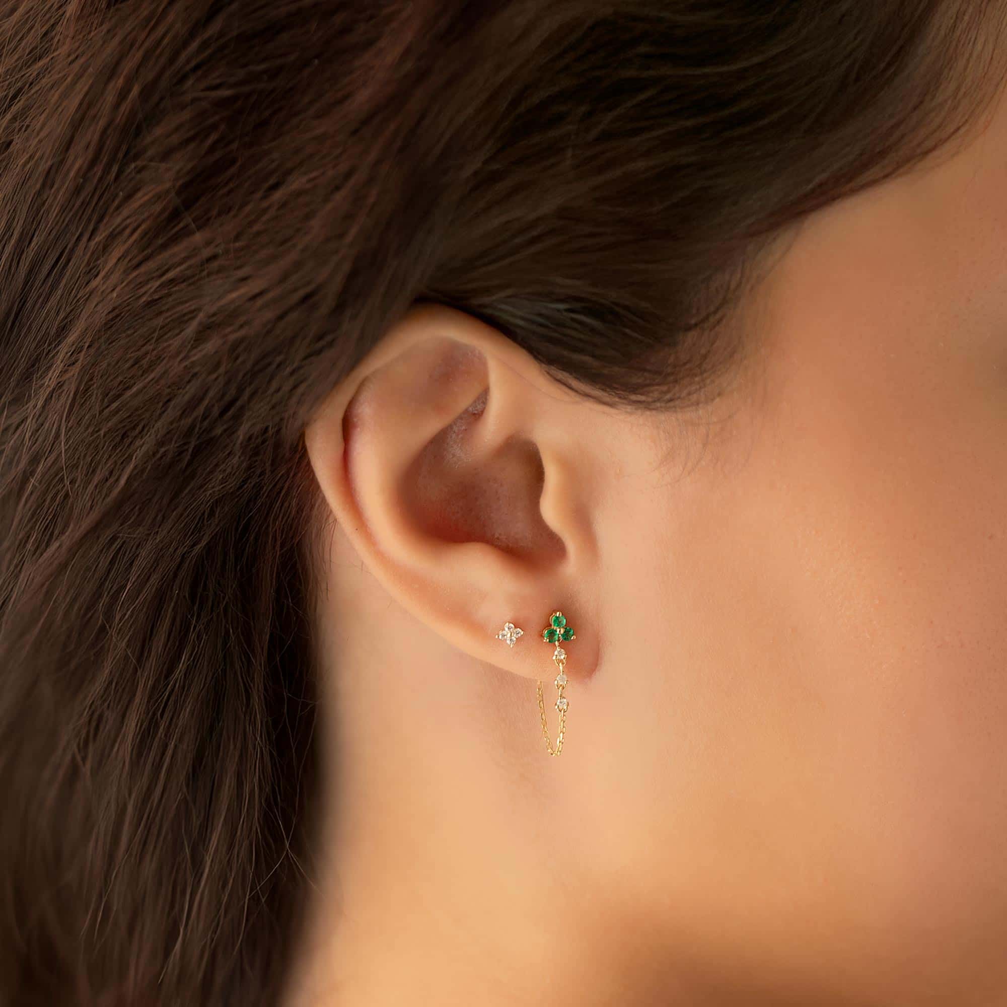 14K gold studs with clear and green stones and a dangling chain, shown on a model's ear
