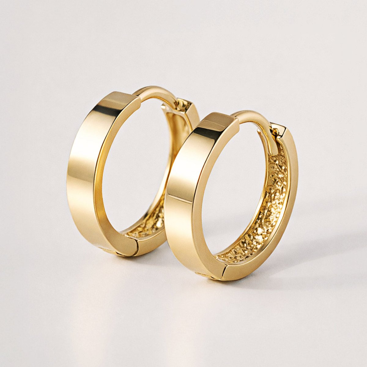 14K gold flat boyfriend huggie hoops with hinged closures, angled pair on a white background