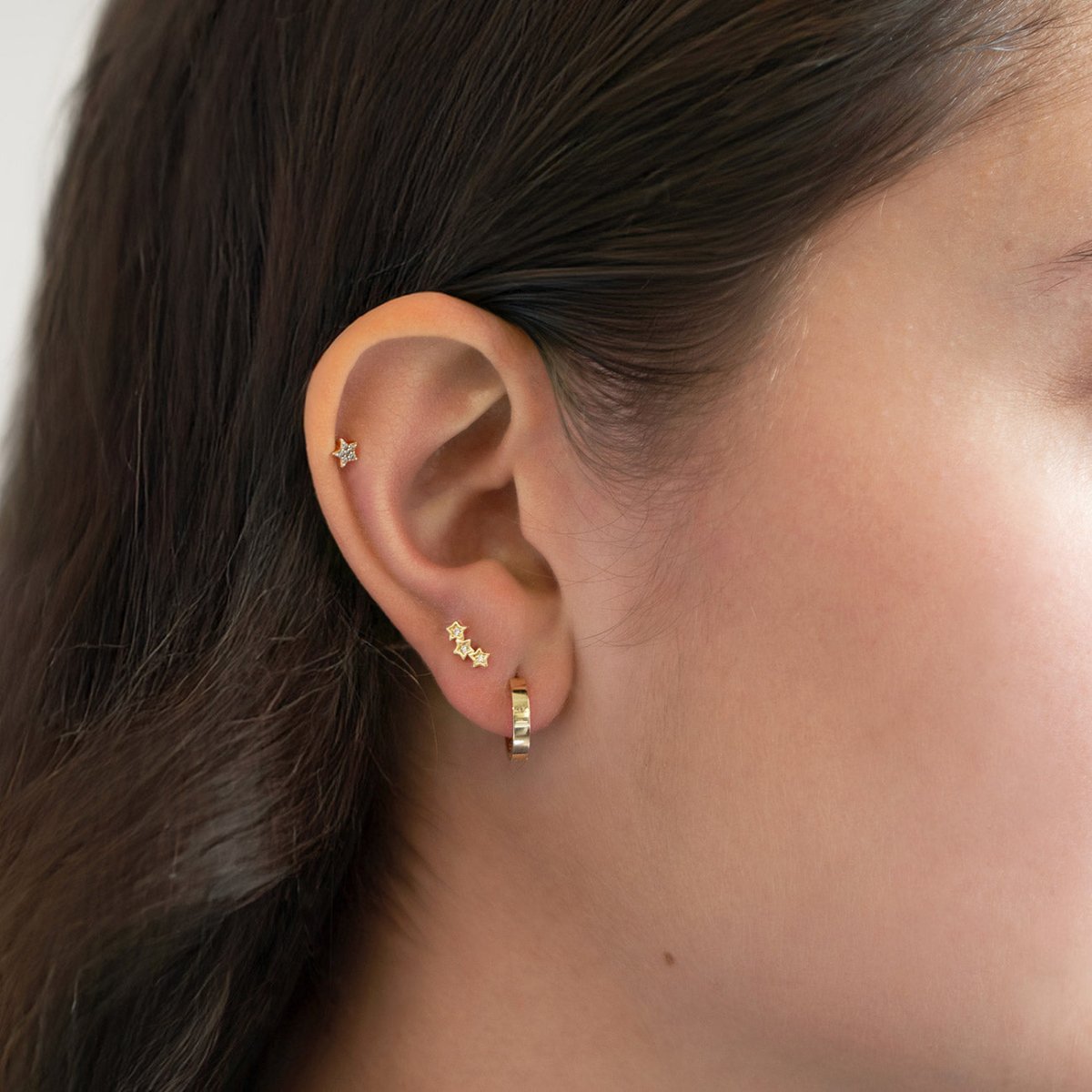 14K gold three-star climber studs with tiny clear stones, shown on a model's ear stack
