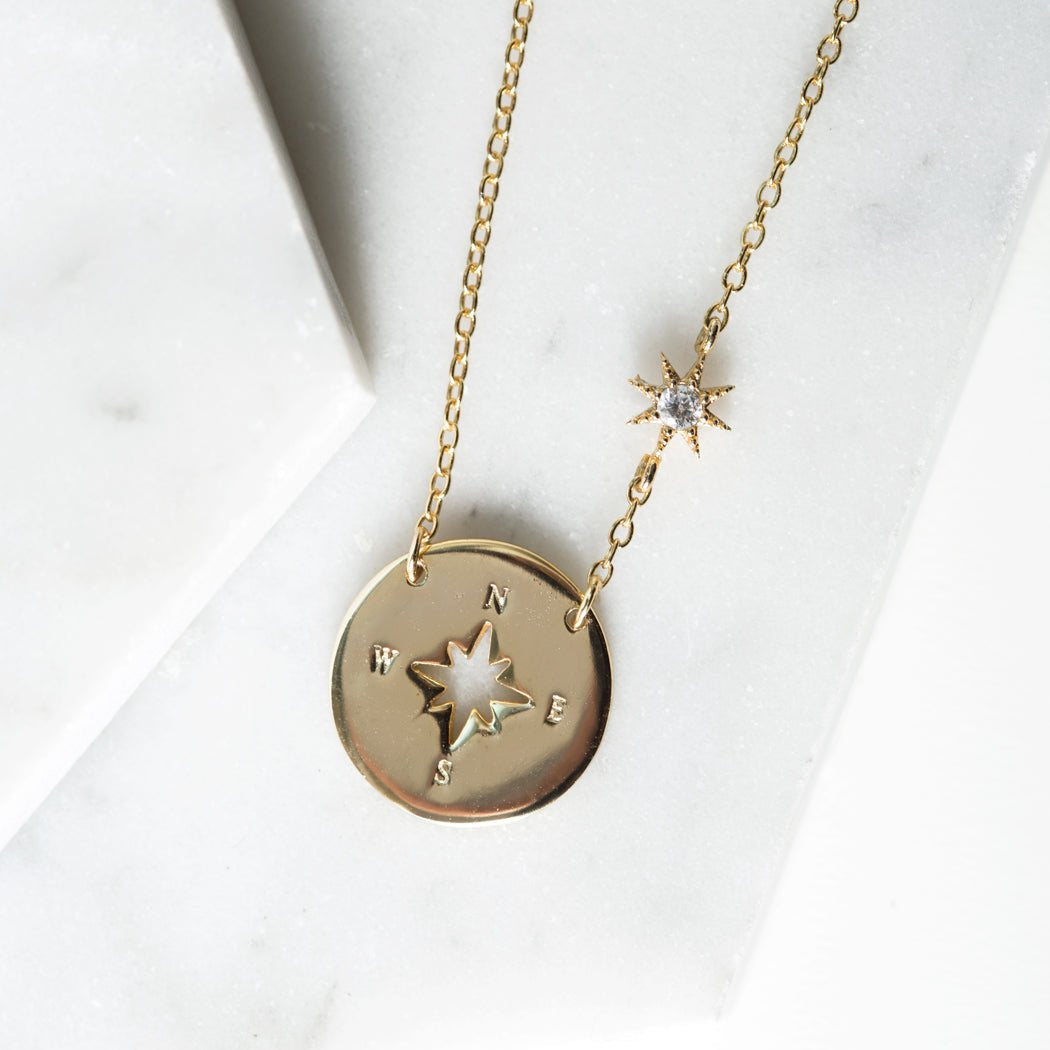 Gold vermeil compass disc necklace with star cutout and clear stone station, on white marble