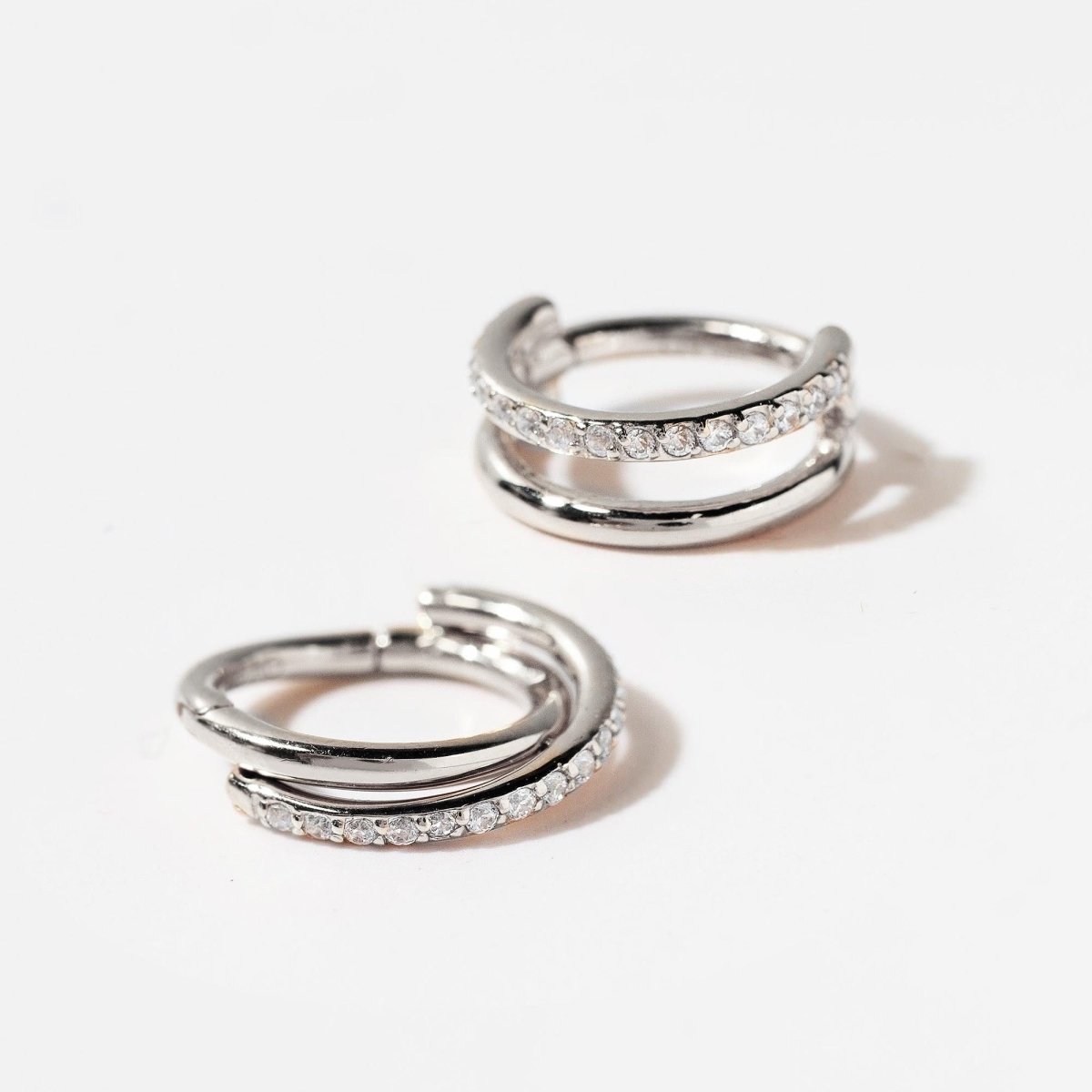 Pair of silver double-hoop pavé cartilage clicker earrings with clear stones, on a white background