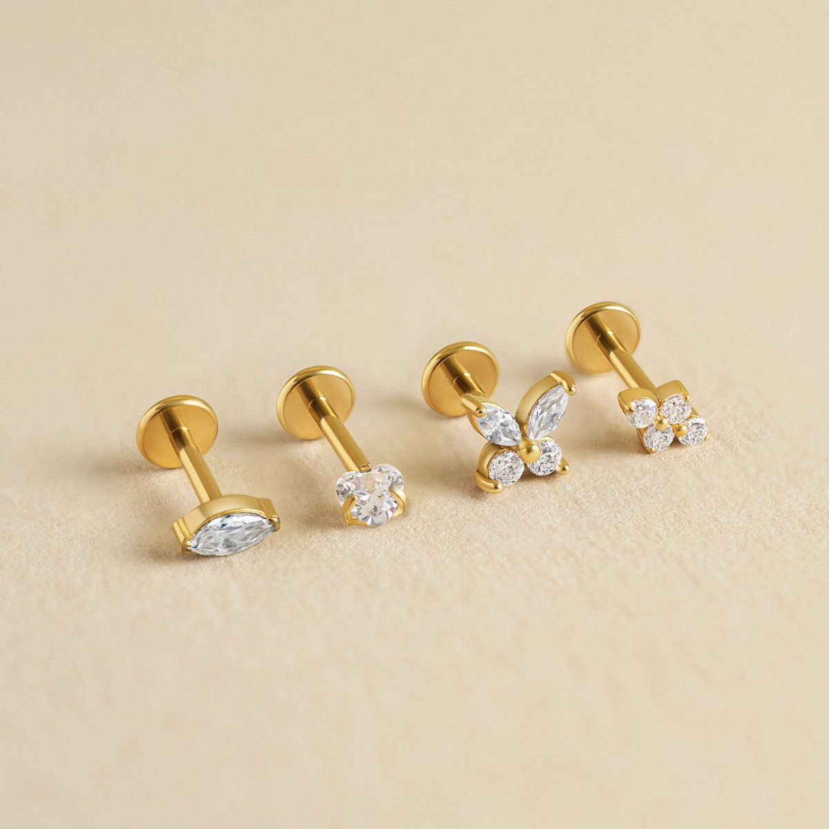 Four gold flat back stud earrings with clear stones in marquise, round and cluster shapes, on a cream background | #Gemstone_White Zirconia